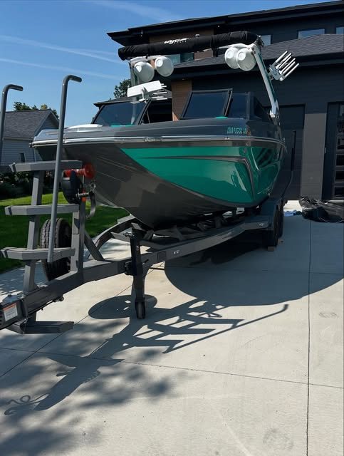 A teal and black wake boat on a lift